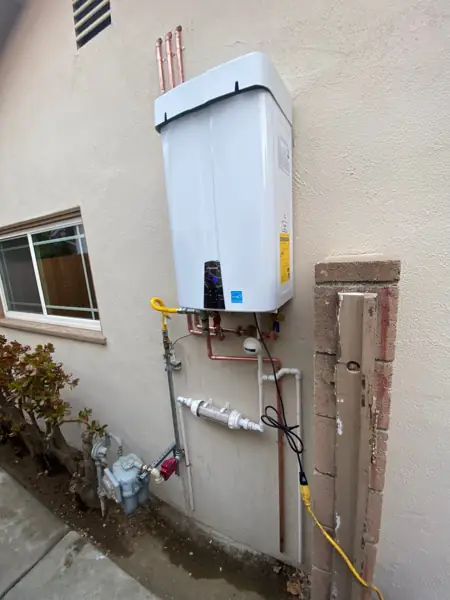 Navien tankless water heater mounted on an exterior wall with copper piping and gas line in Canoga Park