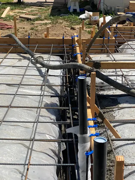 Concrete being poured around wrapped plumbing stub-ups on a new foundation in North Hollywood