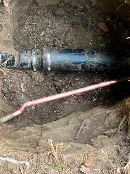 Repaired sewer line with a new pipe section and shielded couplings, with a copper water line below