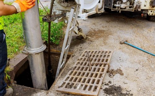 A dirty drain on the ground near a pole.