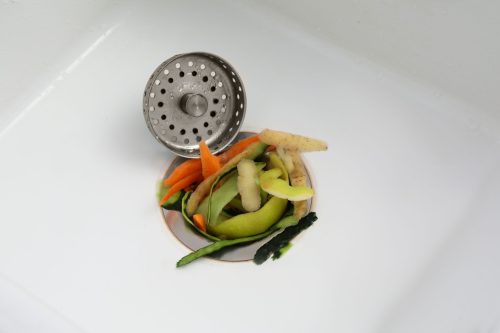 A bowl of vegetables and a strainer on the sink.